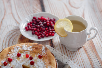 Cheesecake with cranberries and sugar, green tea and lemon on wooden table