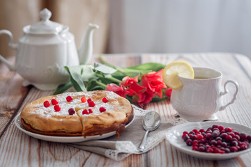 Cheesecake with cranberries and sugar, green tea and lemon on wooden table