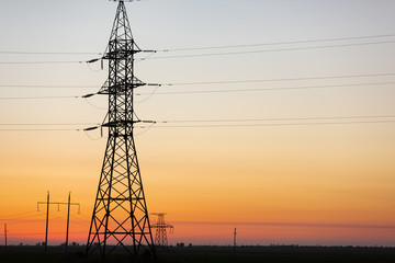 Fototapeta premium a large electrical tower with high-voltage wires, against the background of the dawn sky, in the background are several electric poles, concept