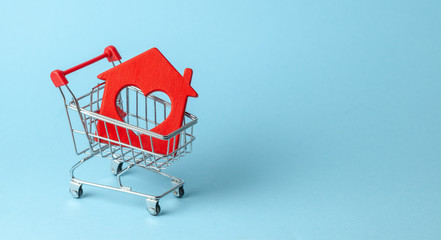 Shopping cart and house on a blue background. Buying and selling real estate. Copy space for text.