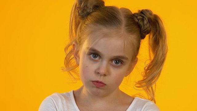 Offended little child angrily looking into camera against orange background whim