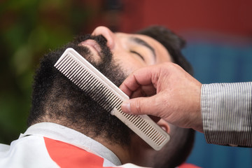 Barber making beard hairstyle using comb at barber shop .
