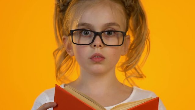 Little smart kid in eyeglasses reading encyclopedia shocked by interesting facts