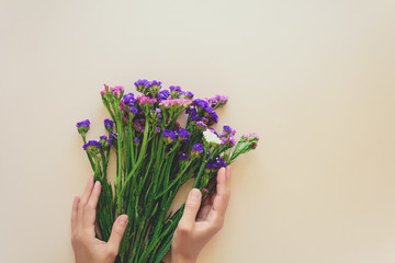 Feminine hands holding bouquet of sea lavender flowers (Limonium) on pink background. Top view. Copy space