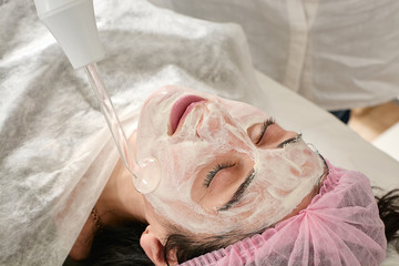 Young woman in beauty salon does rejuvenating, toning procedure darsonval on the face. Medical...