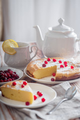 Cheesecake with cranberries and sugar, green tea and lemon on wooden table