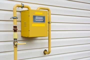 Close-up of metal steel gas meter box with connecting yellow pipes hanging on exterior house wall. Construction, renovation, measurement tool and energy saving concept