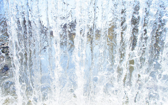 Transparent blue white water pours from above. View through the water wall of the waterfall for the background. © Payllik