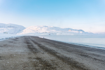 lonely person on a sandy beach in winter on the far north, around mountains and hills in white snow