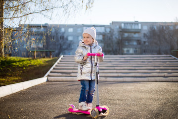 little girl riding a scooter in the Park on a Sunny spring day. Active leisure and outdoor sport...