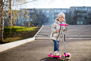 little girl riding a scooter in the Park on a Sunny spring day. Active leisure and outdoor sport...