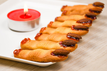 Homemade backed spooky Halloween witch finger cookies covered with sweet cherry blood on a white plate with red candle