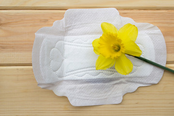 Obraz na płótnie Canvas Sanitary napkin and yellow flower on a wooden table.