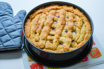 Freshly baked sweet and crunchy homemade cherry pie on a kitchen counter with lattice top and backing glove at side