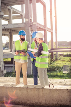 Small group of architects and civil engineers meeting on a construction site. Discussing project details and checking work progress