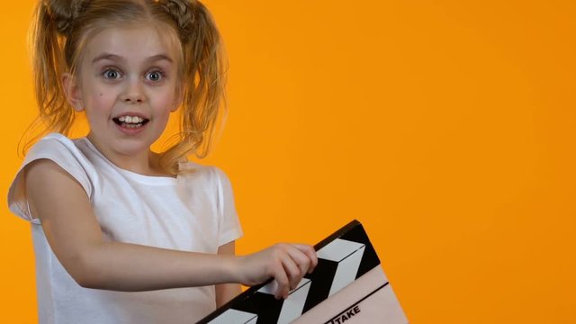 Funny little kid using clapboard and smiling on camera, junior acting school