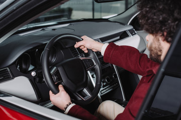 selective focus of curly driver holding steering wheel while sitting in car