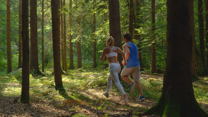 Obraz premium Unrecognizable woman in white sportswear and boyfriend jog through the forest.