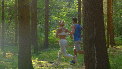 Healthy woman takes her boyfriend for a run in the scenic sunlit spruce forest.