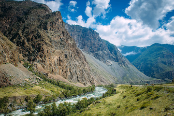 River among the high mountains. Picturesque landscape of rocky Altai mountains and Chulyshman river. Mountain range, river, green coast, blue sky and white clouds.