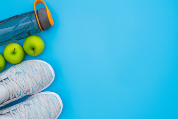 Fitness and healthy active lifestyle background concept.  Training sneakers,  water bottle and green apples on blue table background. Top view with space for your advertisement text.