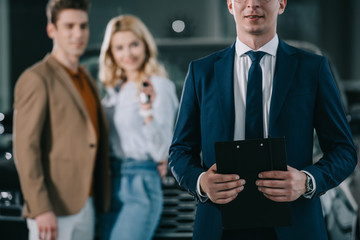 cropped view of car dealer holding clipboard near man and woman