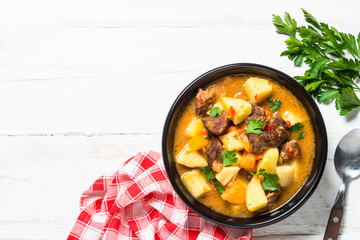 Goulash with meat and vegetables on white wooden table.