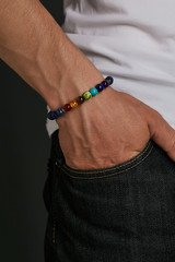 Cropped closeup half-turn shot of man's hand with versicolor stony bracelet with semiprecious...