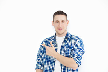 A stylish unshaven man in a shirt points to a copy of the space on a white wall, as something nice shows, has a smiling look, advertises a product. Look here! People, advertising, emotion concept