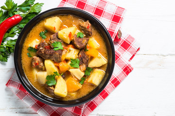 Goulash with meat and vegetables on white wooden table.