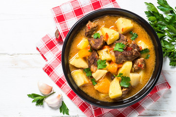 Goulash with meat and vegetables on white wooden table.