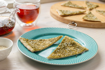 Italian flatbread focaccia with basil pesto sause and sesame seeds on a white table with tea