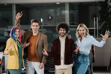 happy group of friends gesturing near automobile in car showroom