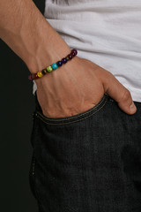 Cropped half-turn shot of guy's hand with stony bracelet with different multicolor stones. The man...