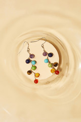 Top view closeup shot of long dangle earrings, adorned with multicolored stony pendants. The...