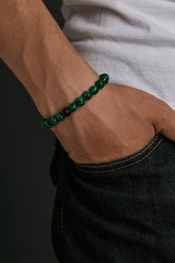 Cropped closeup shot of guy's hand with stony bracelet with smooth surface on the malachite beads....