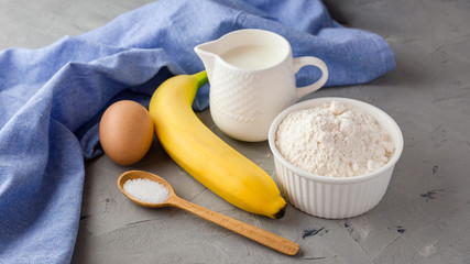The ingredients for the banana cake on gray background. Wooden Spoon, Banana, Eggs, Milk