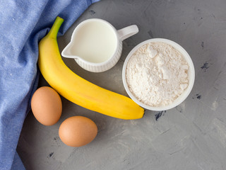 The ingredients for the banana cake on gray background. Wooden Spoon, Banana, Eggs, Milk