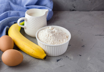 The ingredients for the banana cake on gray background. Wooden Spoon, Banana, Eggs, Milk