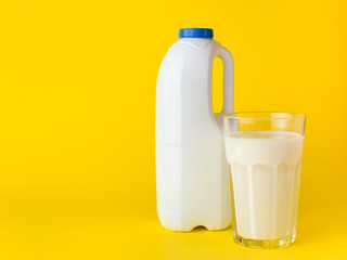 Bottle with fresh milk with handle and glass of milk on yellow background. Mock up for brand template.