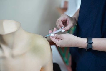 Nursing student practicing blood taking on mannequin hand under instructor supervision