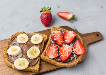 Toast with chocolate and fruits on a wooden board. Strawberries and bananas on stone kitchen table background. Top view