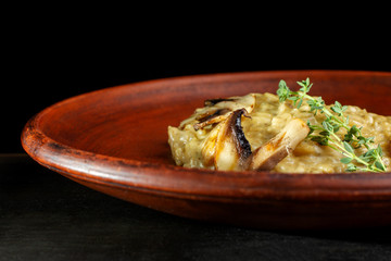 Wheat porridge with mushrooms on a black background in a clay plate.