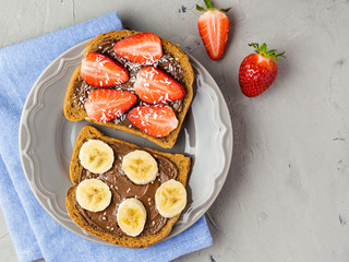 Toast with chocolate and fruits on a gray plate. Strawberries and bananas on stone kitchen table background. Top view
