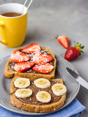 Toast with chocolate and fruits on a gray plate. Strawberries and bananas on stone kitchen table background. Top view
