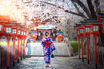 Back view of asia woman with kimono and Japanese umbrella against sakura flower background.