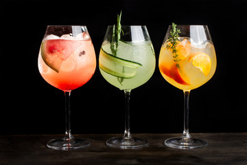 Three alcoholic cocktails with orange slices, ice, watermelon slices and cucumbers.