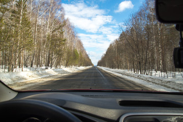 View of the road through the windshield. Snow on the sidelines. Wet asphalt road. Blue sky with...