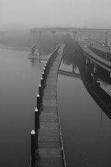 Moody photo of a walking bridge over water with fog in black and white