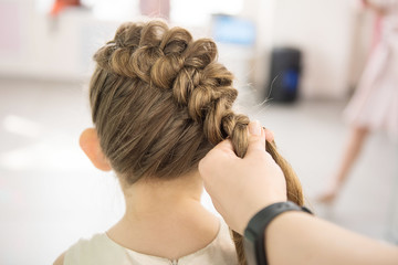 Fototapeta premium Hairdresser weaving plaits in beauty salon. Hairdressing services. Сreating hairstyle. Hair styling process. Children's hairdressing salon.